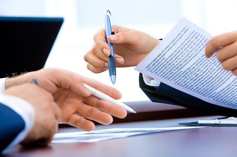 Zwei Personen unterschreiben gemeinsam einen Vertrag mit Stift und Dokumenten auf einem Tisch.