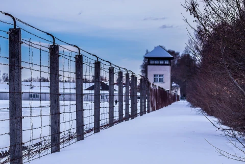 Im Vordergrund ein Stacheldrahtzaun, im Hintergrund Gebäude, Ansicht einer Gedenkstätte (ehemaliges Konzentrationslager), Winter, Schnee