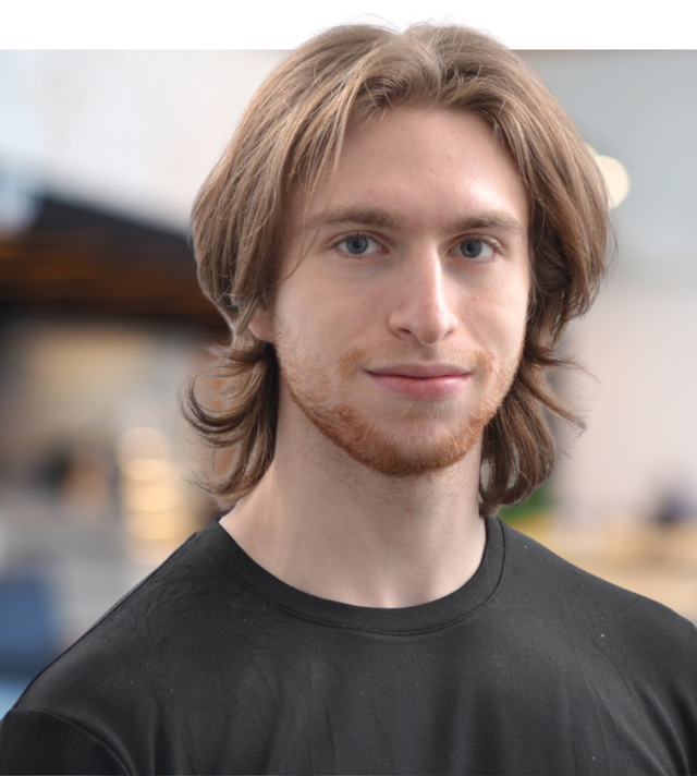 Porträt eines jungen Mannes mit langen Haaren, der lächelt und ein schwarzes T-Shirt trägt.
